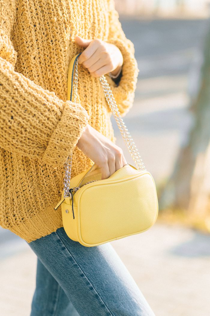 A stylish yellow bag paired with a knitted sweater and denim jeans outdoors.